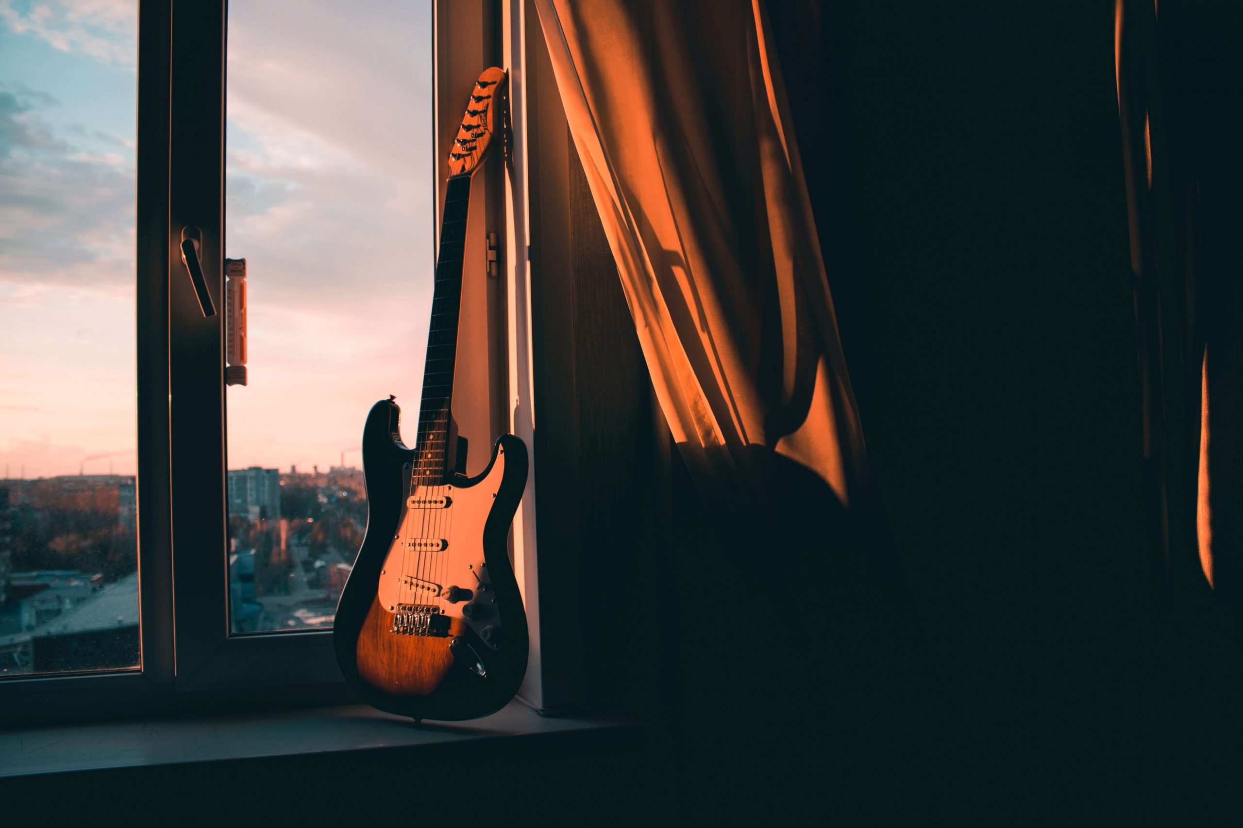 guitare devant une fenêtre et un couché de soleil